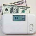 Digital thermostat at 67°F next to a U.S. $100 bill, showing energy-efficient settings for home comfort.