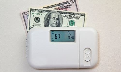 Thermostat with digital display at 67°F and $50, $100 bills, indicating HVAC maintenance and energy efficiency.