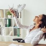Woman in a white blouse holding white shoes in a bright office, representing Barker Heating & Cooling’s comfort services.