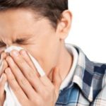Young man in a checkered shirt holding a tissue, showing discomfort related to air quality at Barker Heating & Cooling.
