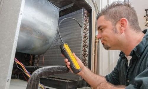 Technician inspecting HVAC cooling unit with measuring tool for performance. Barking Heating & Cooling services in action.