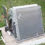 Used air conditioning unit with visible coils and components on grass, representing HVAC maintenance and repair needs.