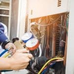 Technician inspecting a refrigeration unit with a pressure gauge and hoses for HVAC maintenance at Barker Heating & Cooling.