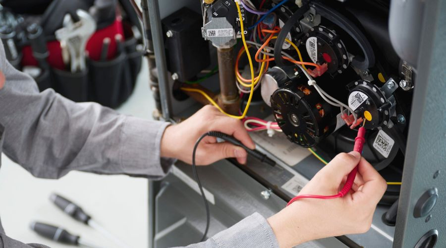 Technician repairing HVAC machinery, using tools and multimeter on control panel with organized components.
