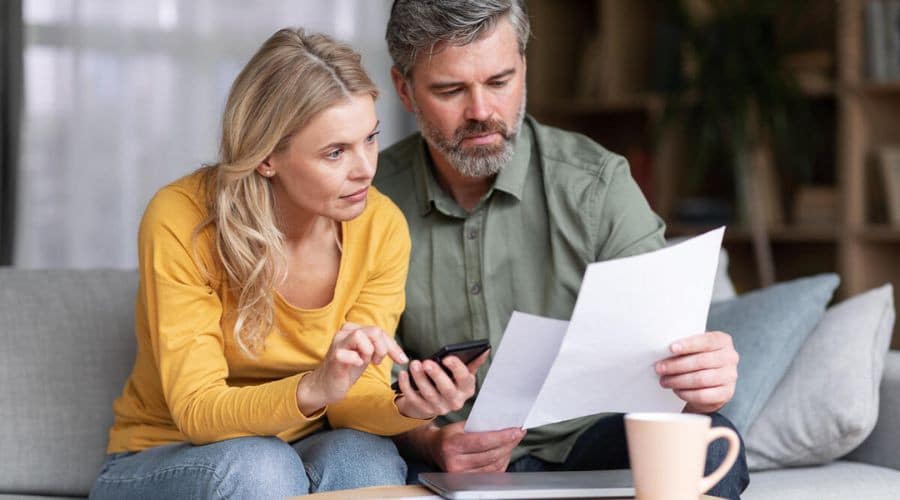 Couple discussing HVAC maintenance strategies with a laptop, smartphone, and documents on a coffee table.