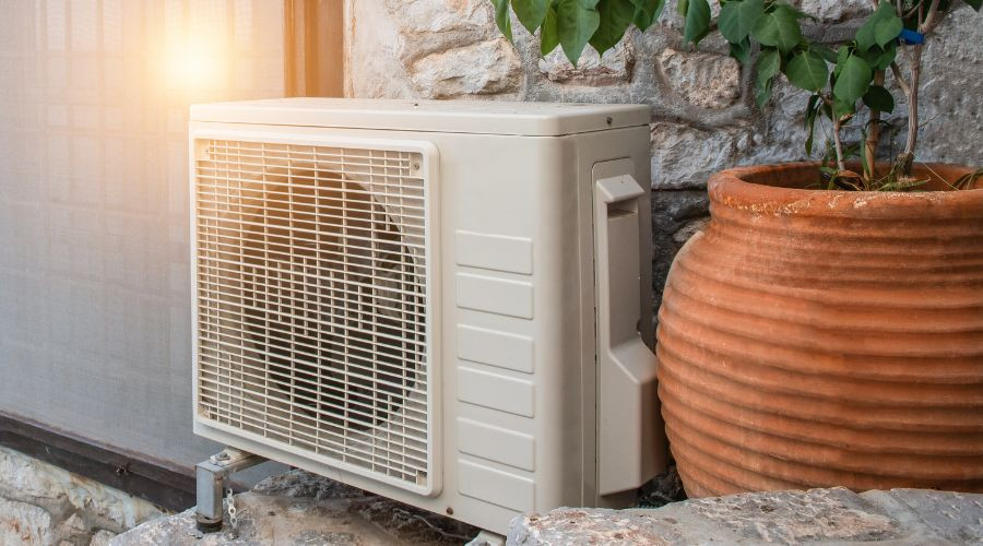 Air conditioning unit and terracotta plant pot on a textured stone wall, enhancing comfort at Barker Heating & Cooling.